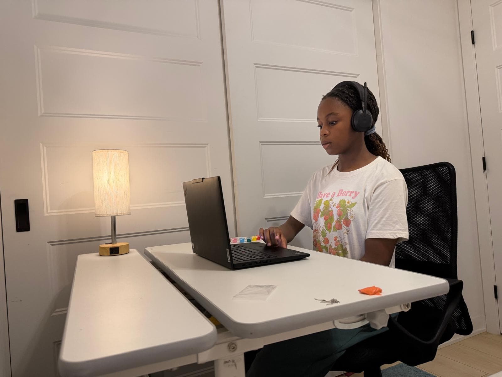A student wearing headphones, learning at a laptop in a home bedroom